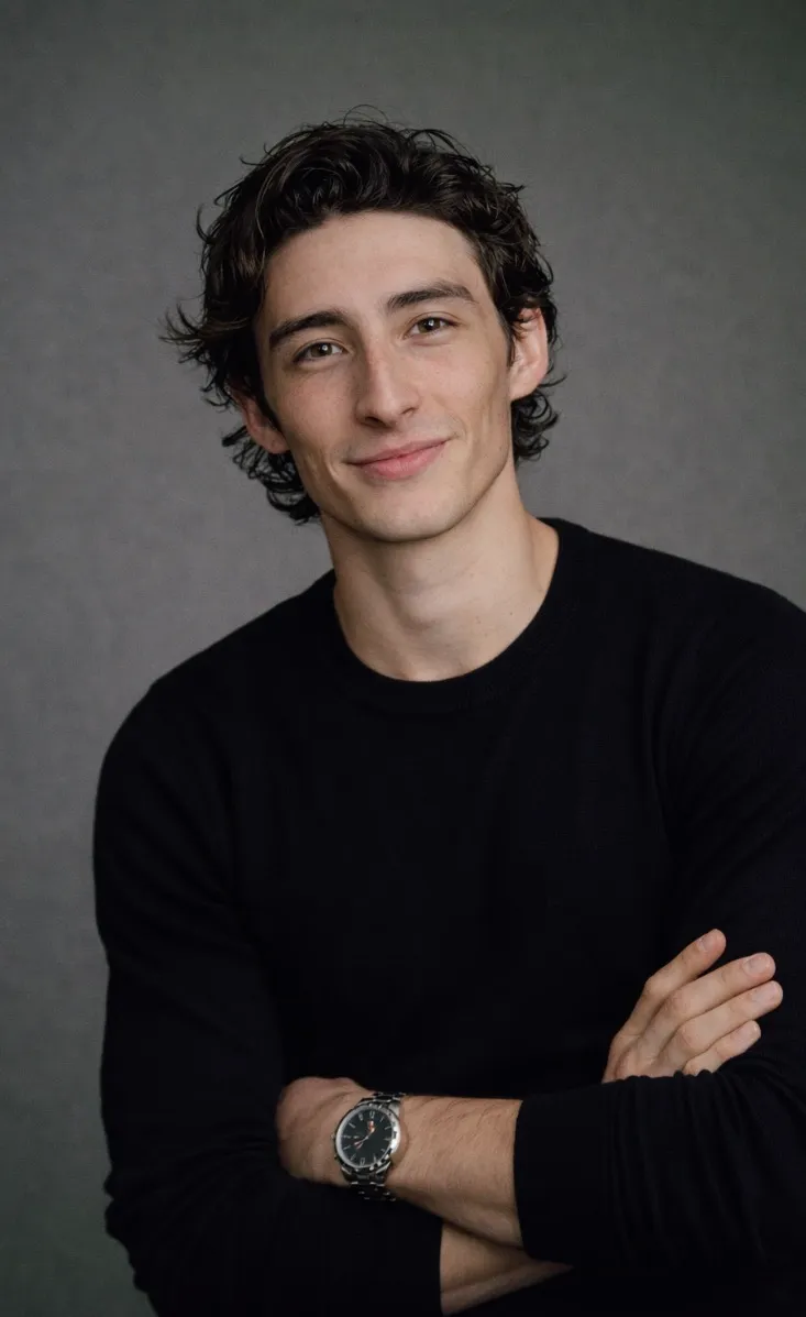 Jackson in a black crew neck sweater, arms folded, against a plain grey studio backdrop